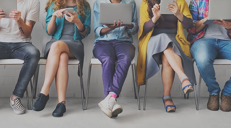 five people sat on chairs looking at different hand held devices